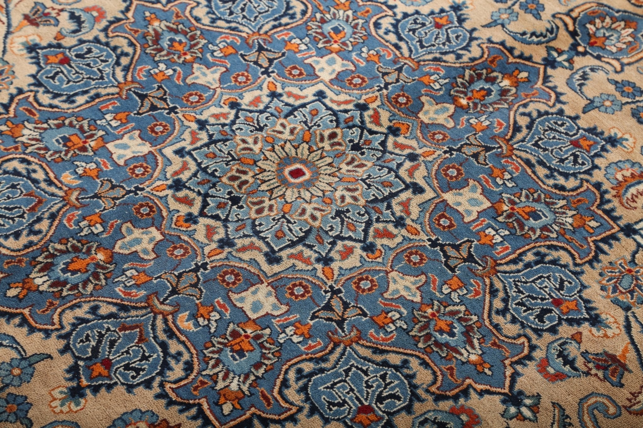 Close-up of blue and tan rug field with dense floral motifs and orange highlights.