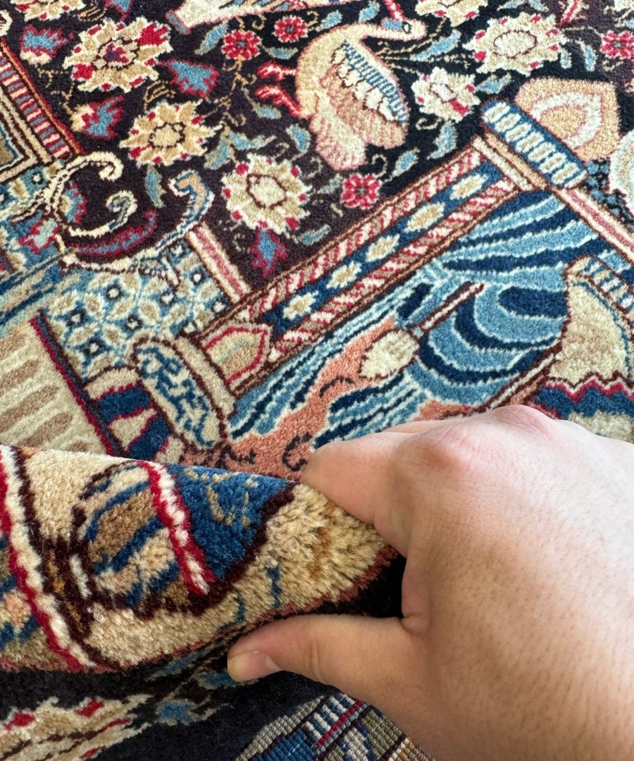 Hand holding fabric corner on Persian Kashmar rug with blue wave pattern border