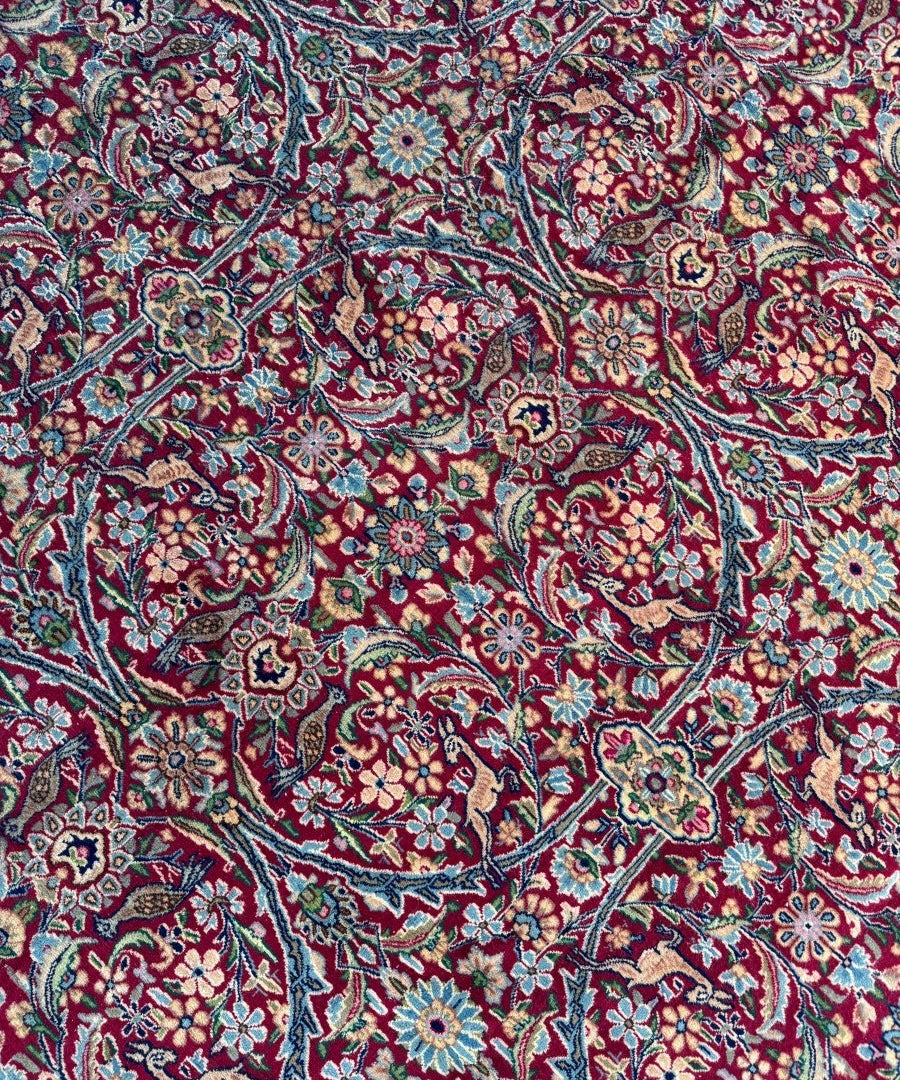Persian Kerman rug close-up with teal ground, red motifs, and small floral accents
