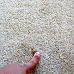 Close-up of off-white rug pile with fingertips showing soft texture