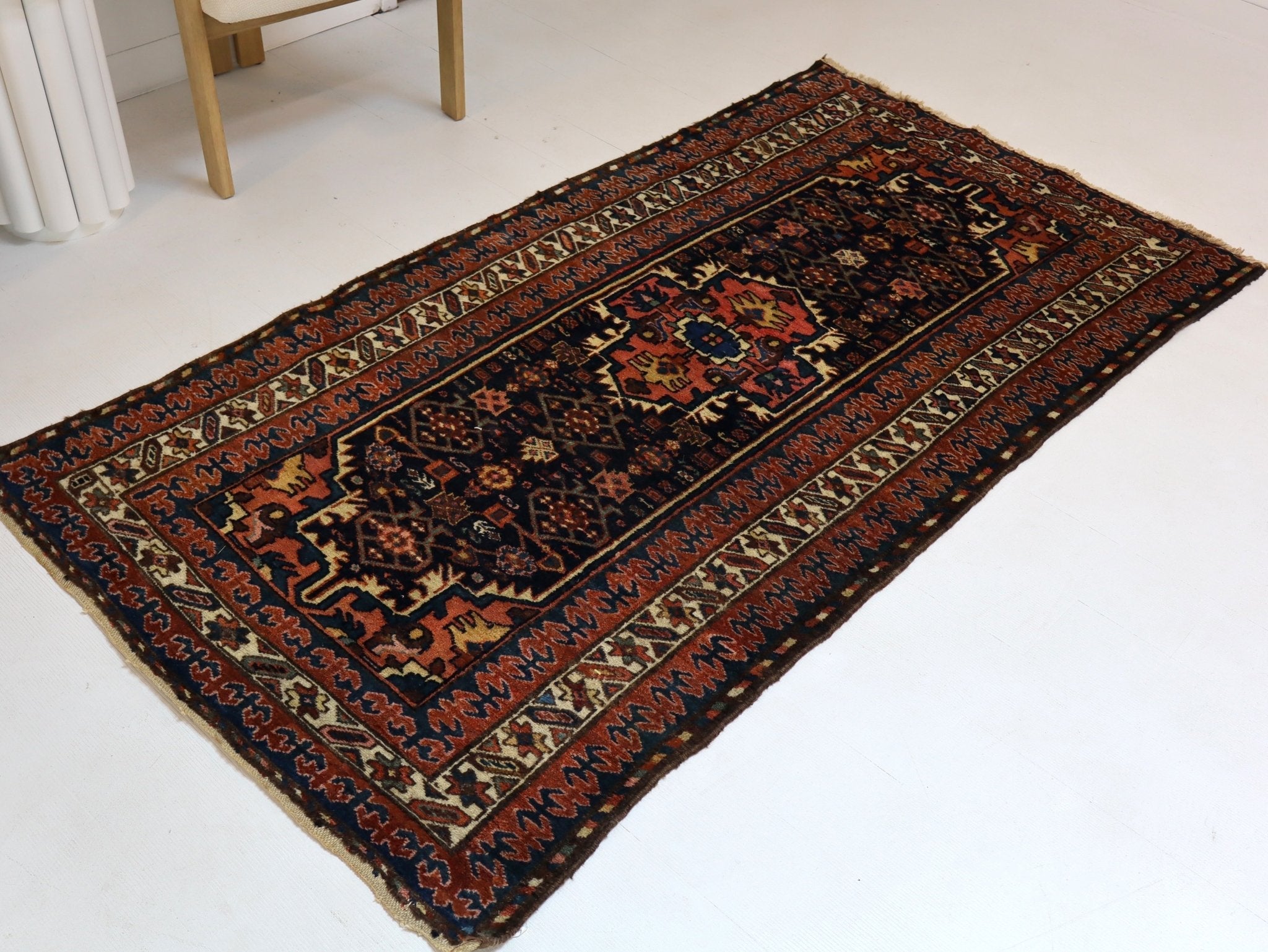 Persian Kurdi rug angled view with navy ground and rust-and-blue decorative frame