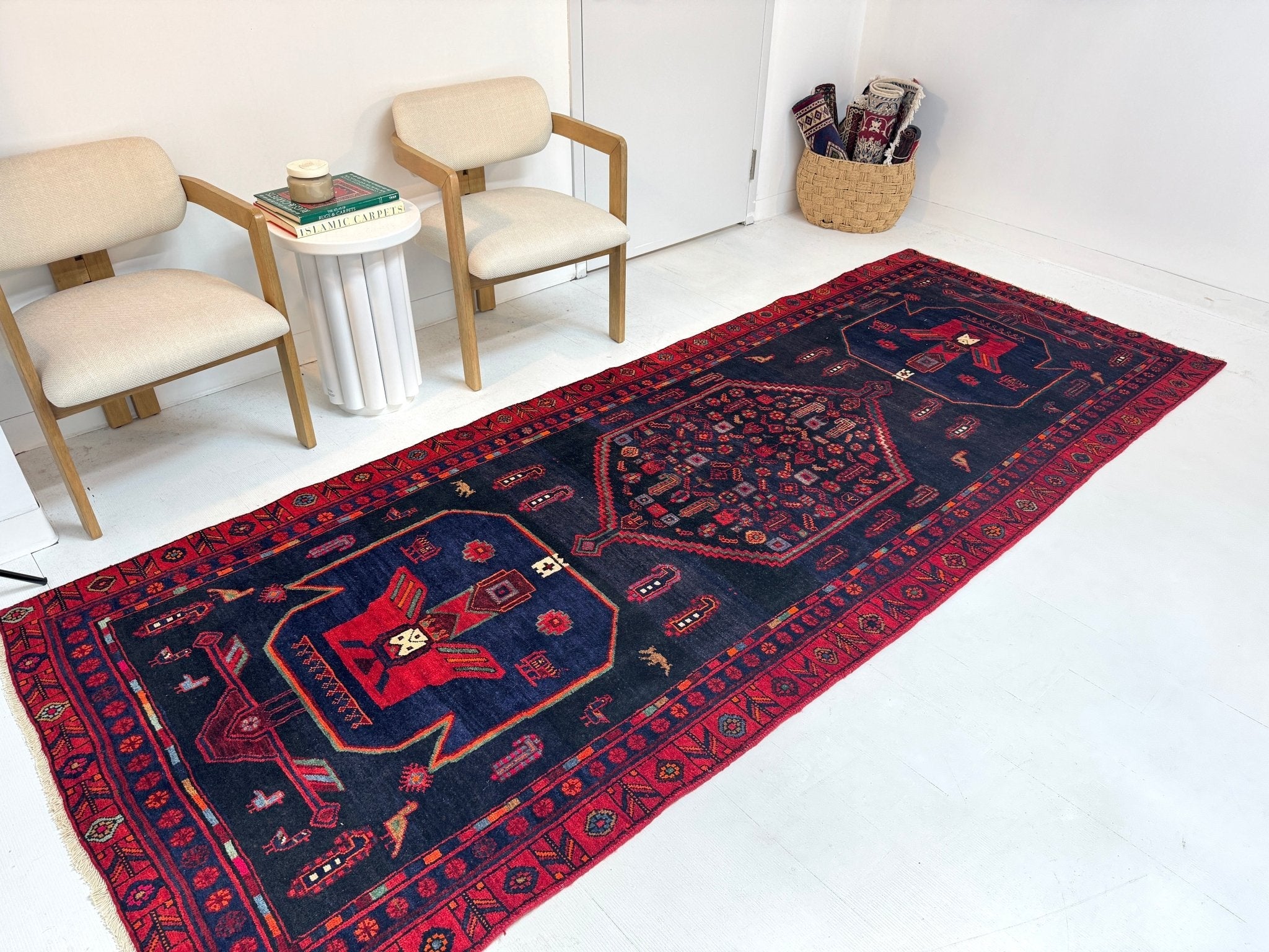 Kurdish Koliai rug laid out, dark navy ground with red border and symmetrical center motifs.