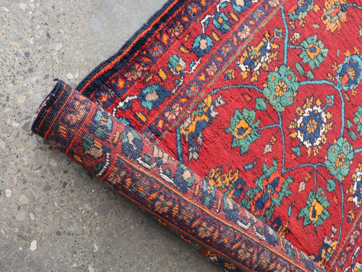 Rolled corner of red runner rug with teal floral motifs and dark blue border