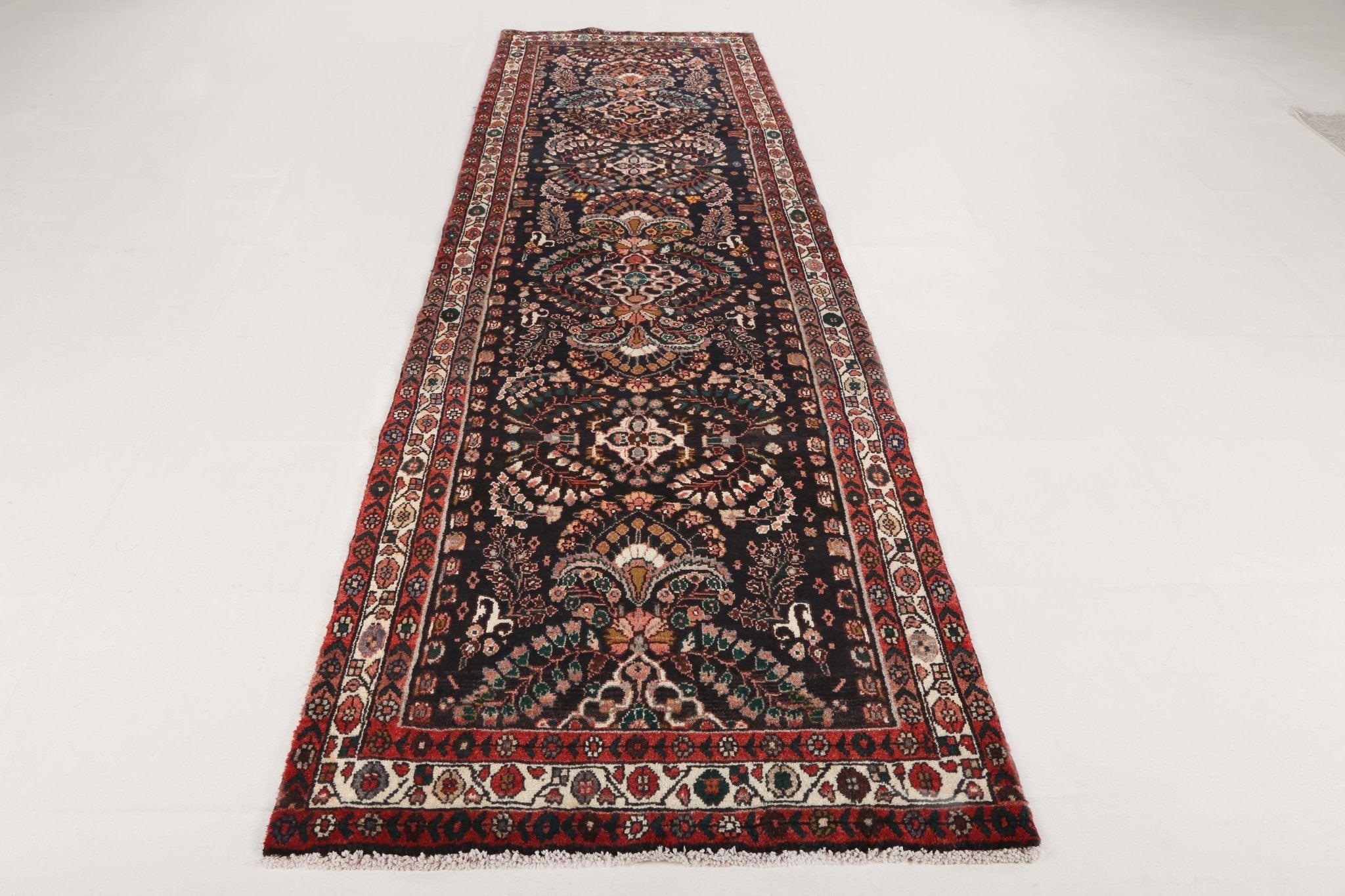 Long runner rug with dark background and intricate red, teal, cream motifs