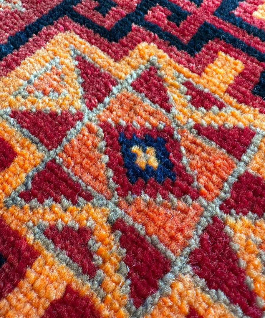 Persian Lori rug close-up, red-orange and blue geometric pattern in textured pile
