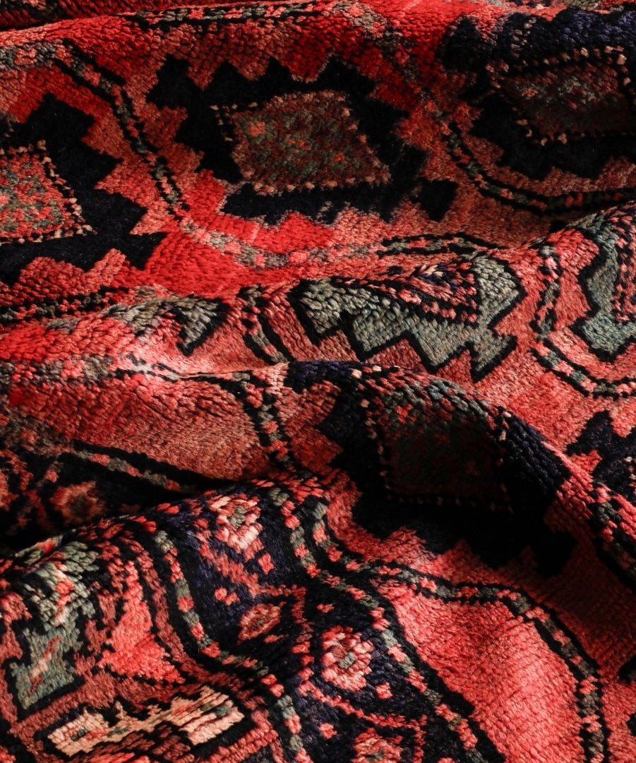 Persian Lori rug texture close-up in red with black and tan ornamental swirls and waves.
