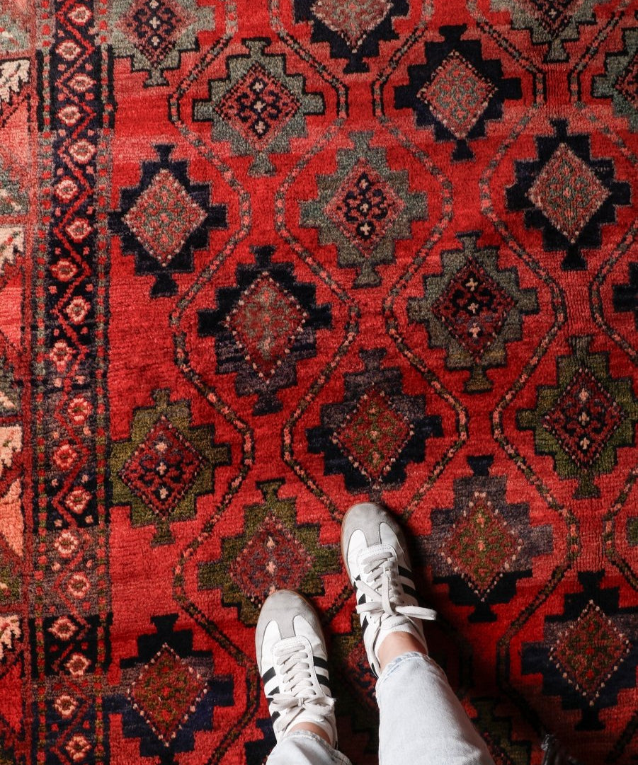 Persian Lori rug close-up with red background and dark blue and black diamond medallions.
