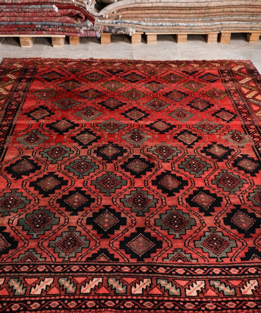 Persian Lori rug with red ground, dark diamond pattern, decorative border and short fringe.