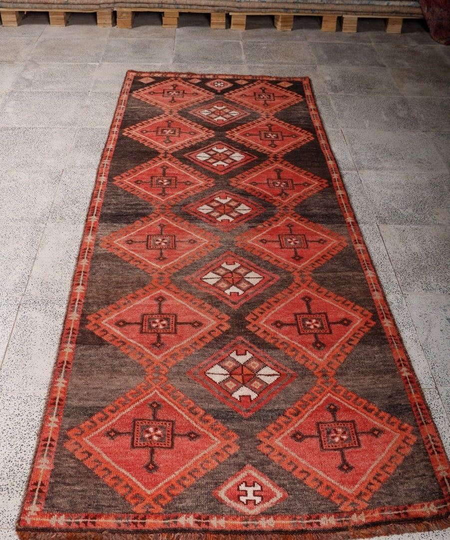 Rectangular runner rug with dark brown field and red repeating medallion and diamond pattern.