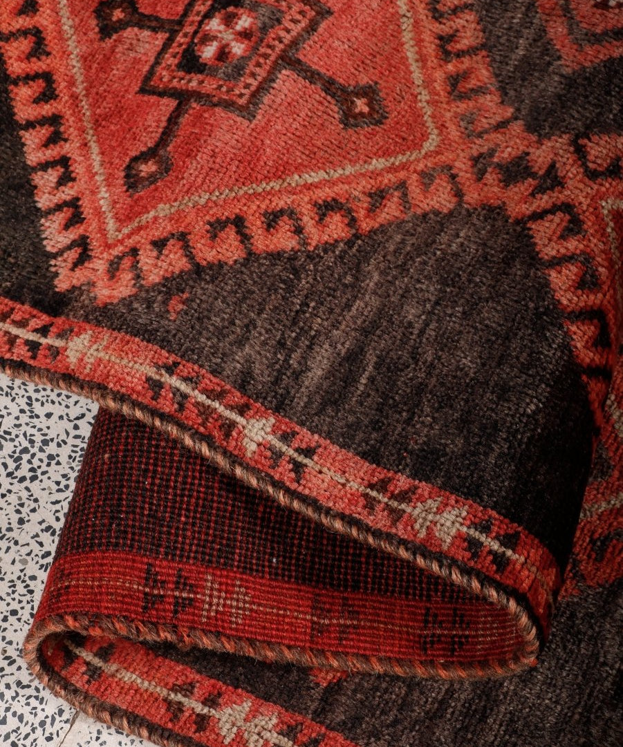 Runner rug edge with dark brown center and red border, folded in a roll view.