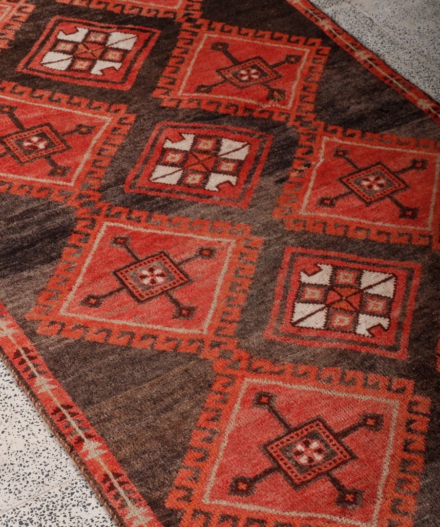 Close-up of dark brown and red rug showing layered geometric squares and border motifs.