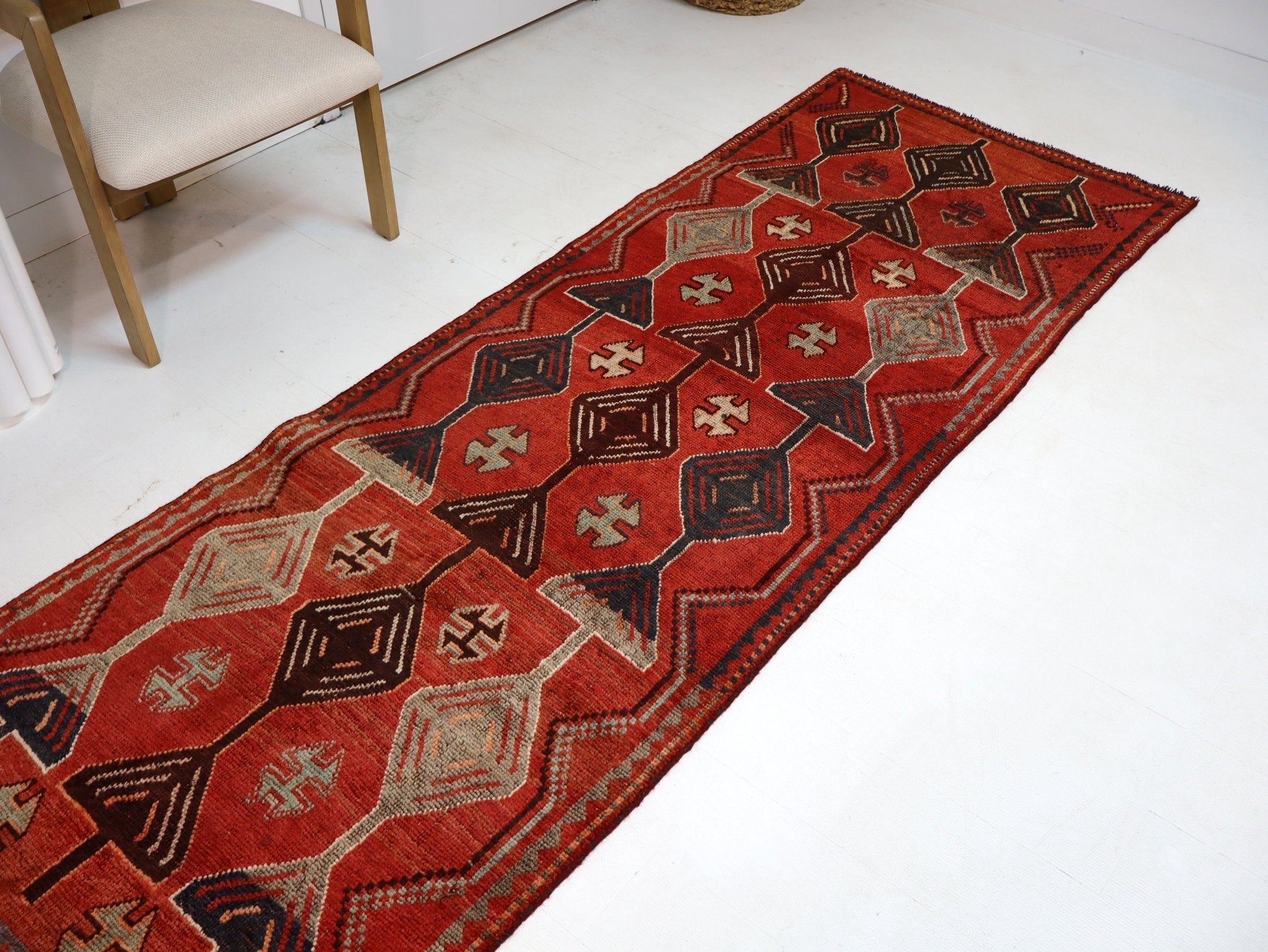 Red geometric runner rug displayed on white floor with chair legs at edges.