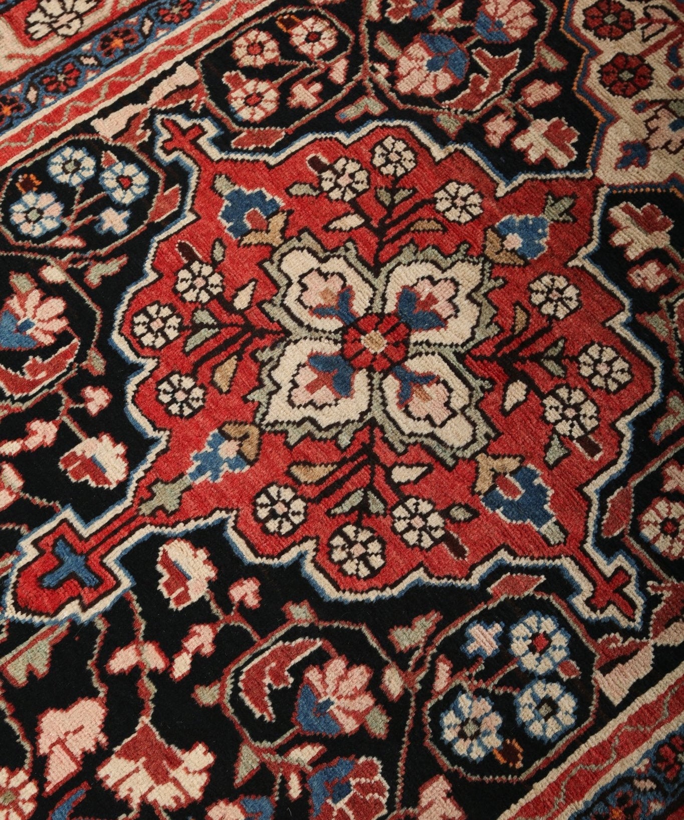Persian-style runner rug close-up with dense floral and geometric pattern in red, navy, beige.