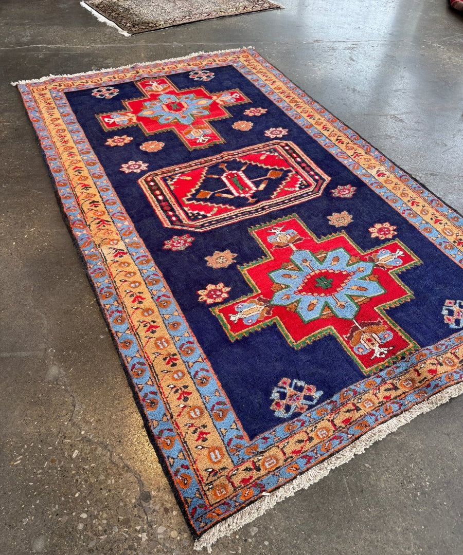 Persian Meshkin rug, diagonal view with navy field, red center medallion, patterned border