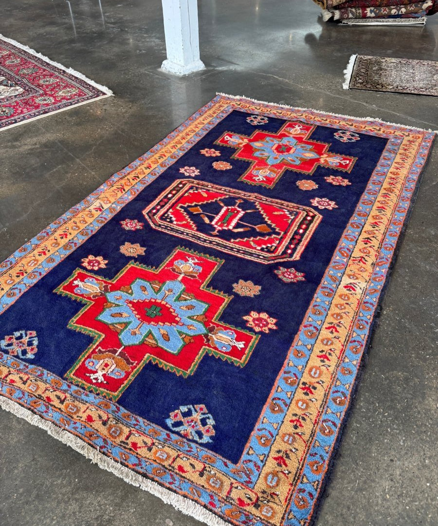 Persian Meshkin rug on floor, navy base with red medallions and geometric corner motifs