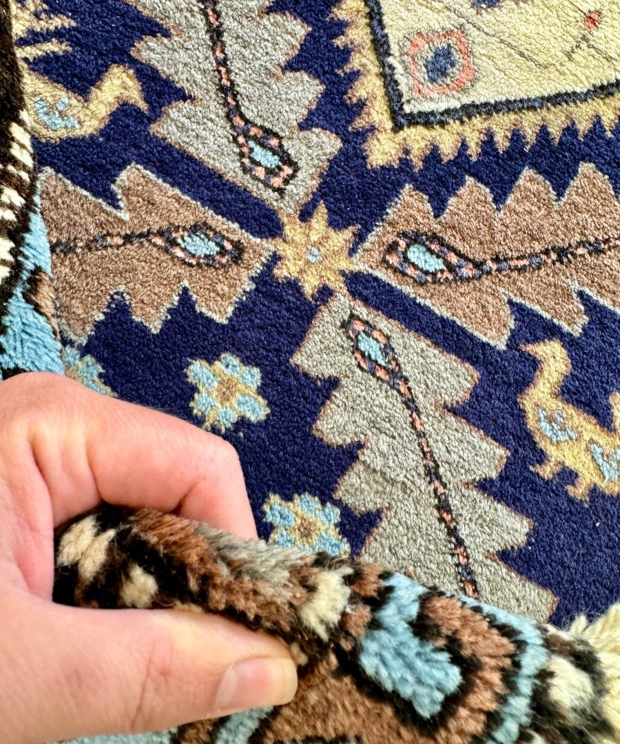 Close-up of Persian Meshkin rug pile with blue field, cream details, and stitched motifs