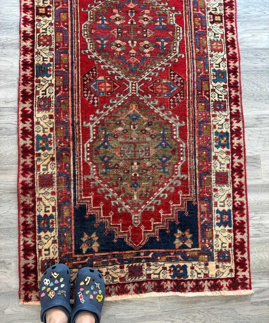Persian Meshkin runner rug with red field, navy border, and cream geometric motifs.