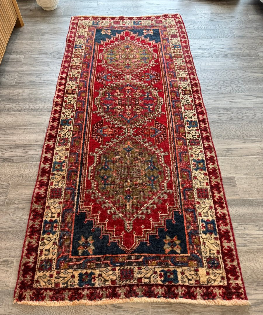 Persian Meshkin runner rug laid flat, red center medallion with blue and cream details.