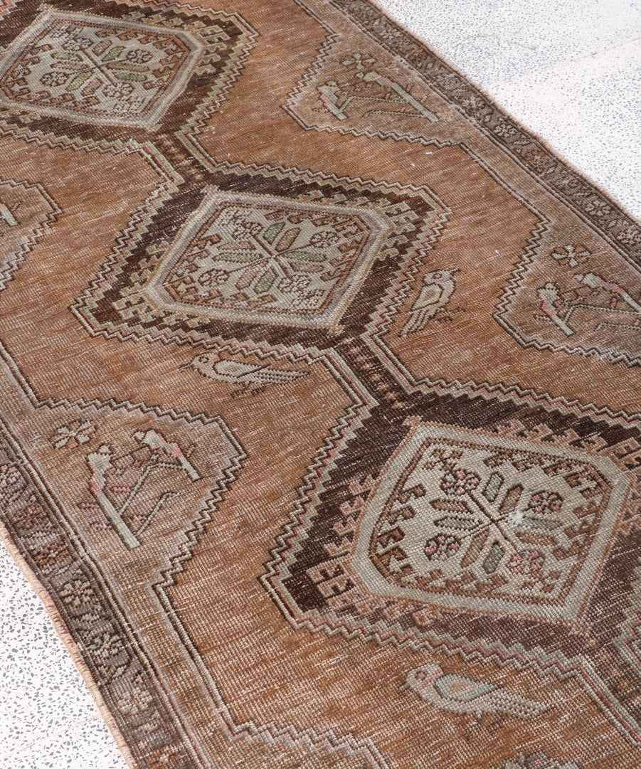 Tan runner rug with repeating square medallions, zigzag accents, and fringed border.