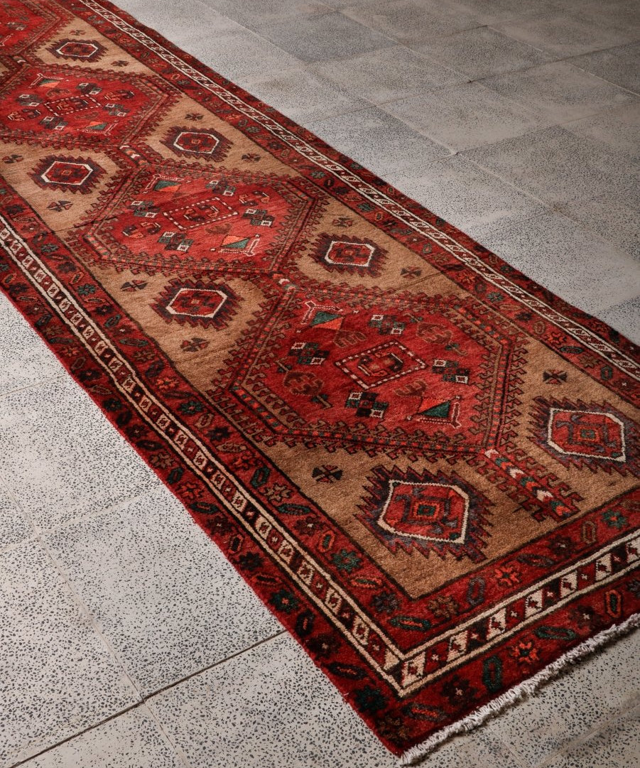 Persian runner rug corner view with red field, beige ground, and repeating diamond border