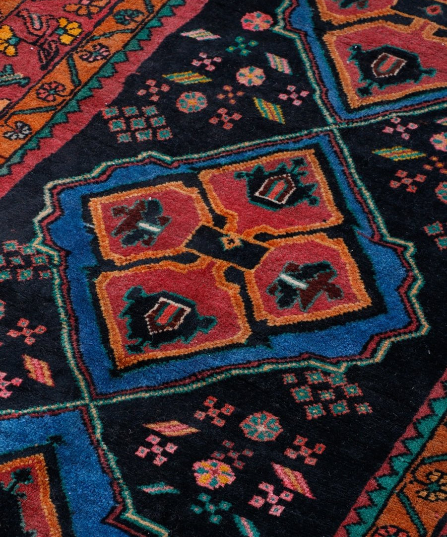 Persian meshkin rug close-up: black background with blue outlined medallions in red, tan, yellow.