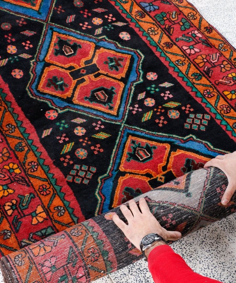 Persian meshkin rug corner close-up with patterned border; dark ground with orange-red accents.