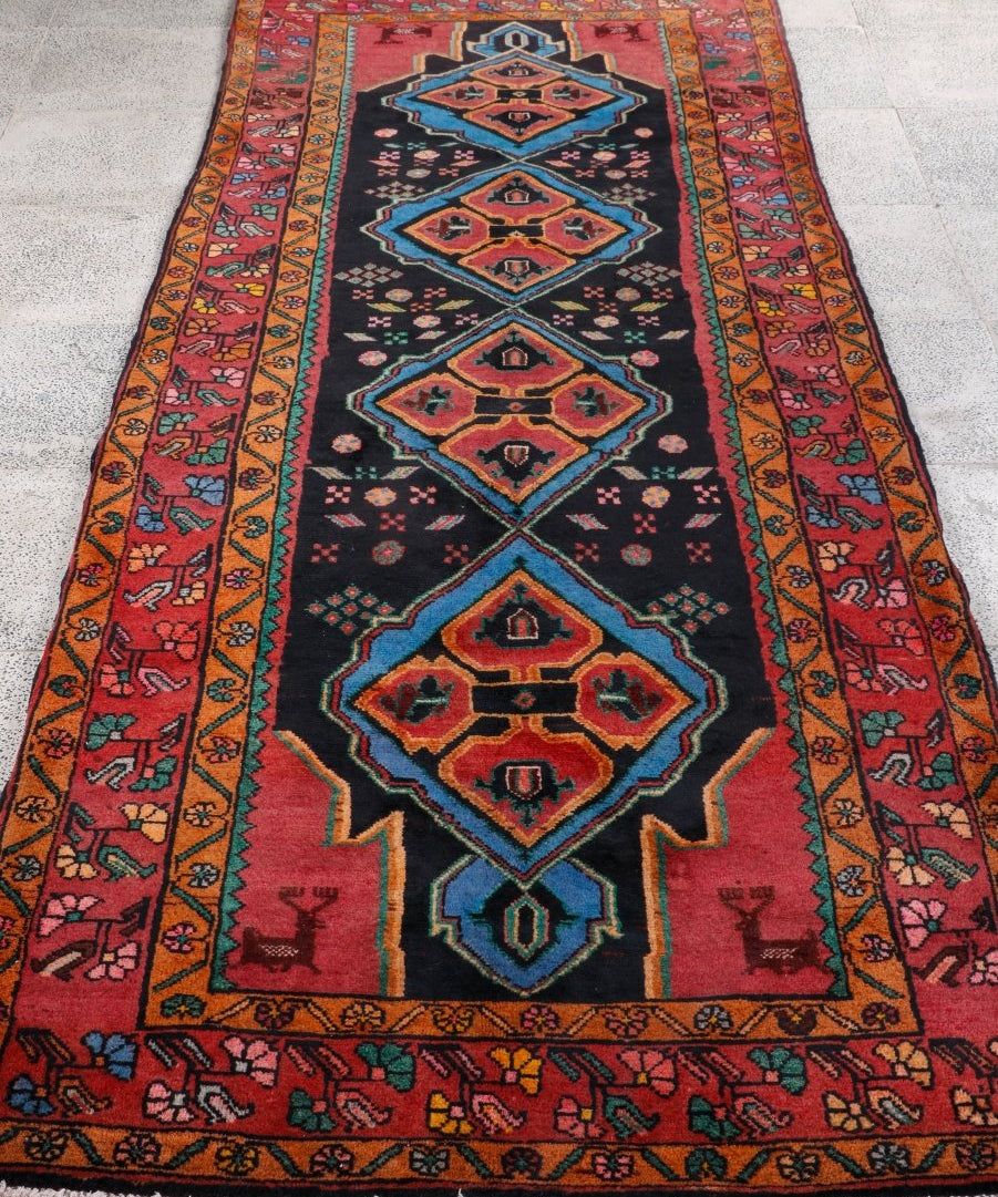 Persian meshkin runner rug, full view: red border, dark center, blue and tan diamond motifs.