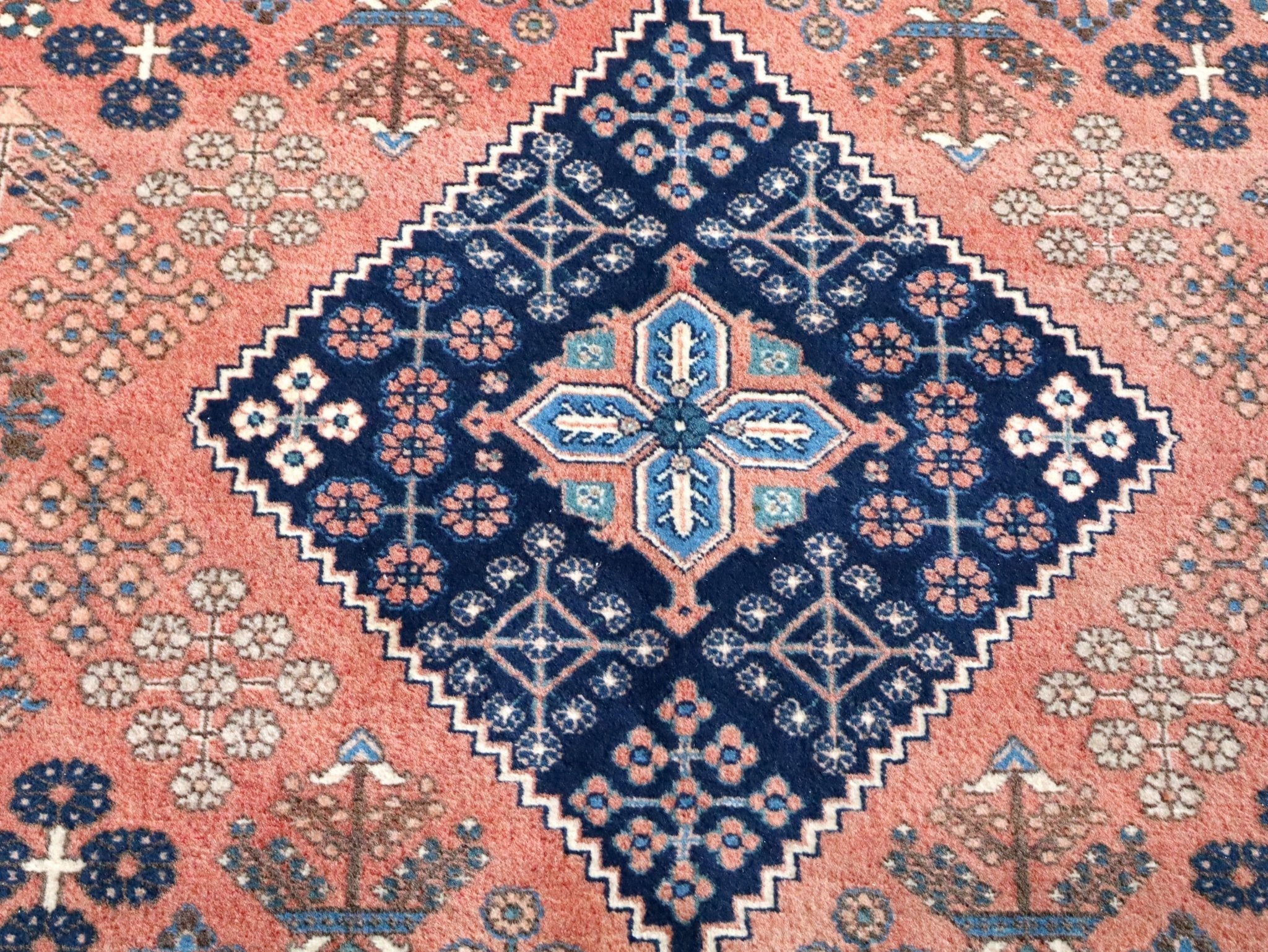 Persian-style rug top view with navy medallion, coral background, and teal accents