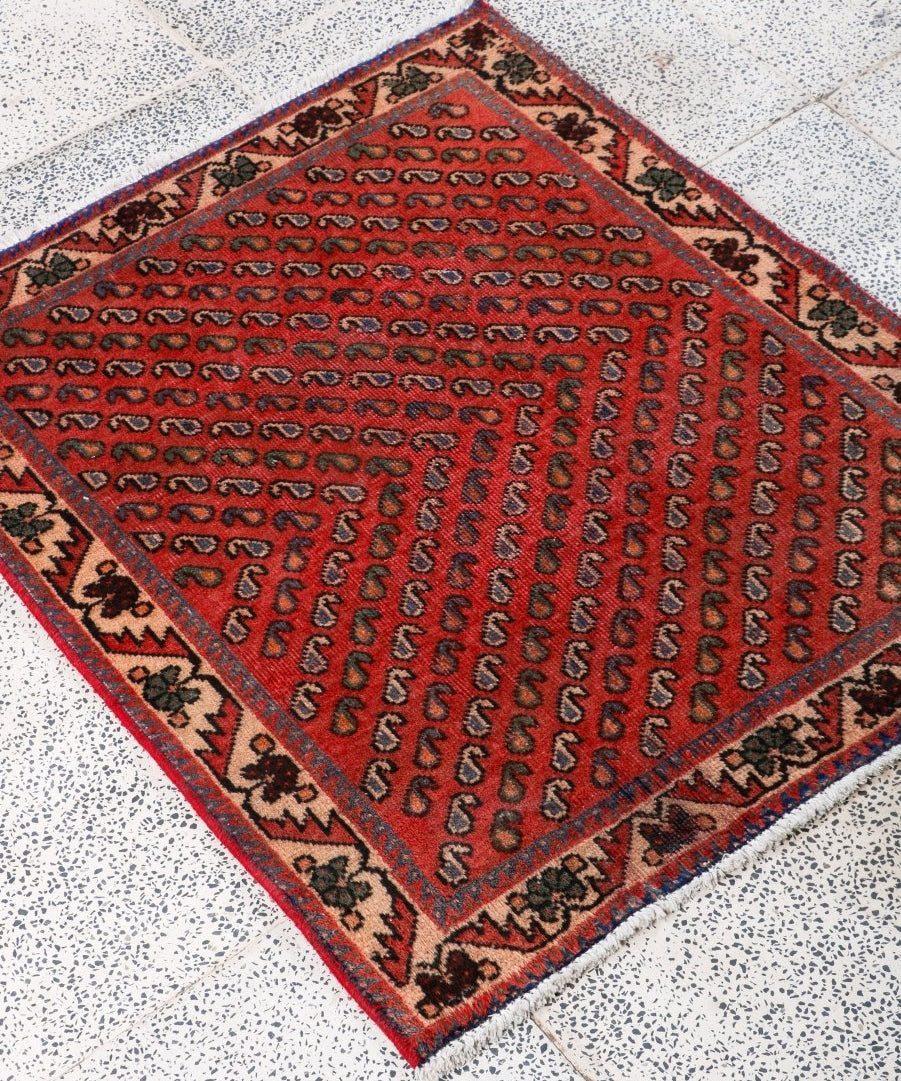 Square red Persian-style rug with repeating motifs and multicolor geometric border.