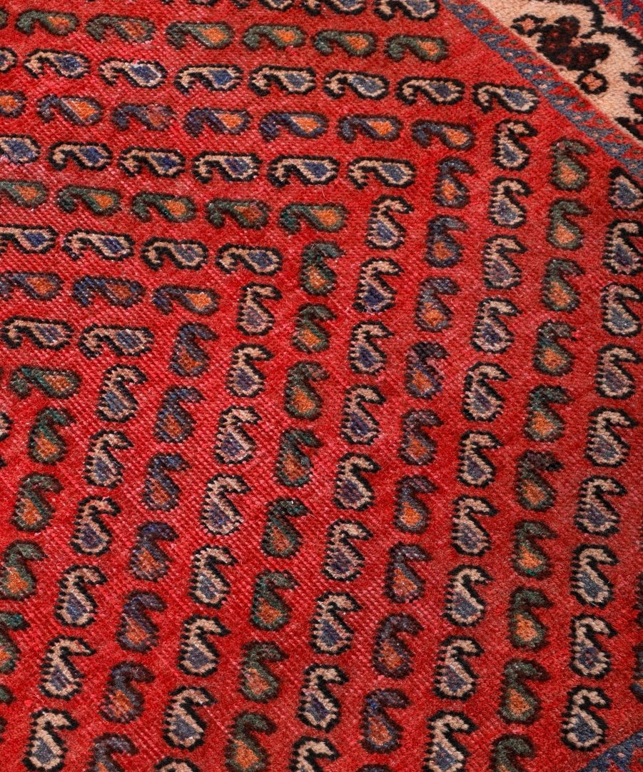 Close-up of red rug field with repeating dark blue and beige motif pattern.