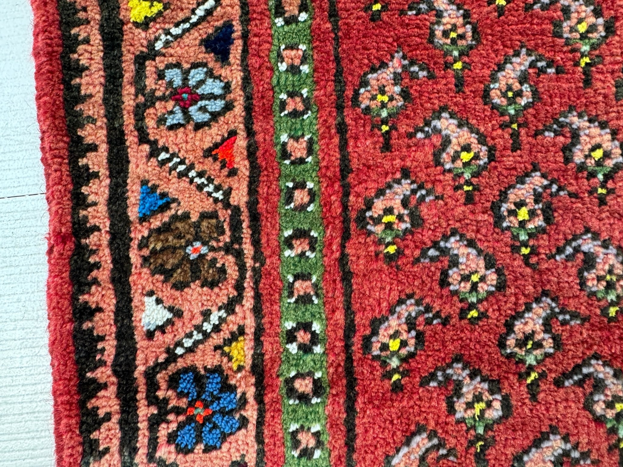Close-up of red runner rug weave with small floral motifs and dark border stripe.