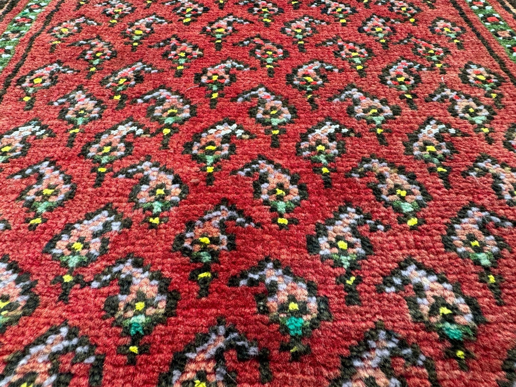 Close-up of red rug surface with repeating floral medallion pattern in green and blue.