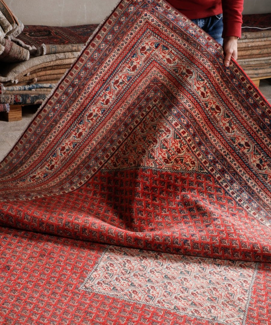 Persian Mir rug shown folded: red ground with cream center medallion and ornate borders.