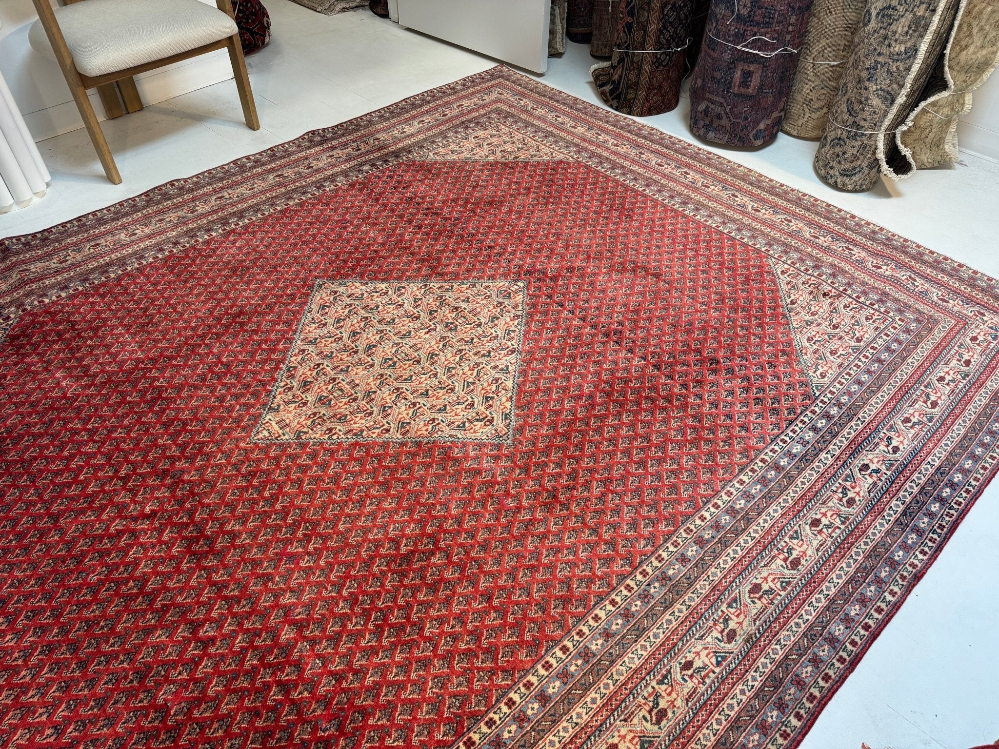 Persian-style rug with red field, beige diamond motif, and ornate multicolor border