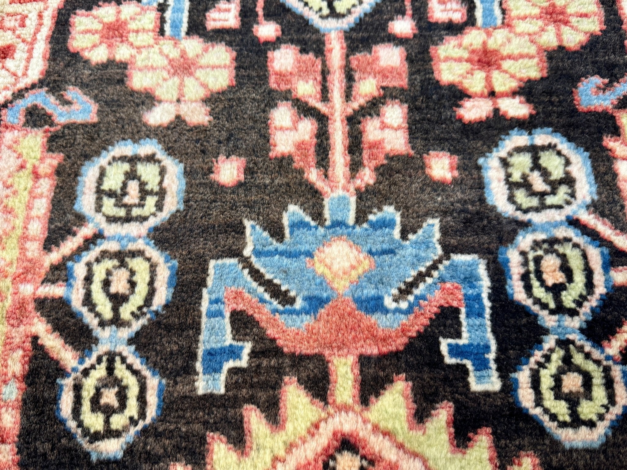 Persian Nahavand rug close-up of black field with blue flower motifs and pink accents