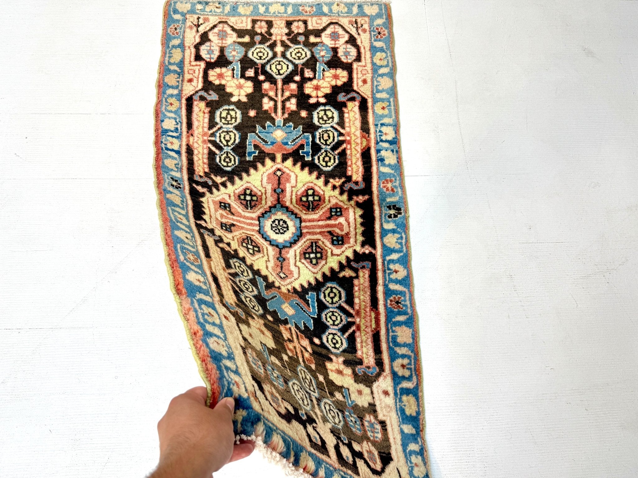 Persian Nahavand rug angled view with hand holding edge; blue border and black motifs