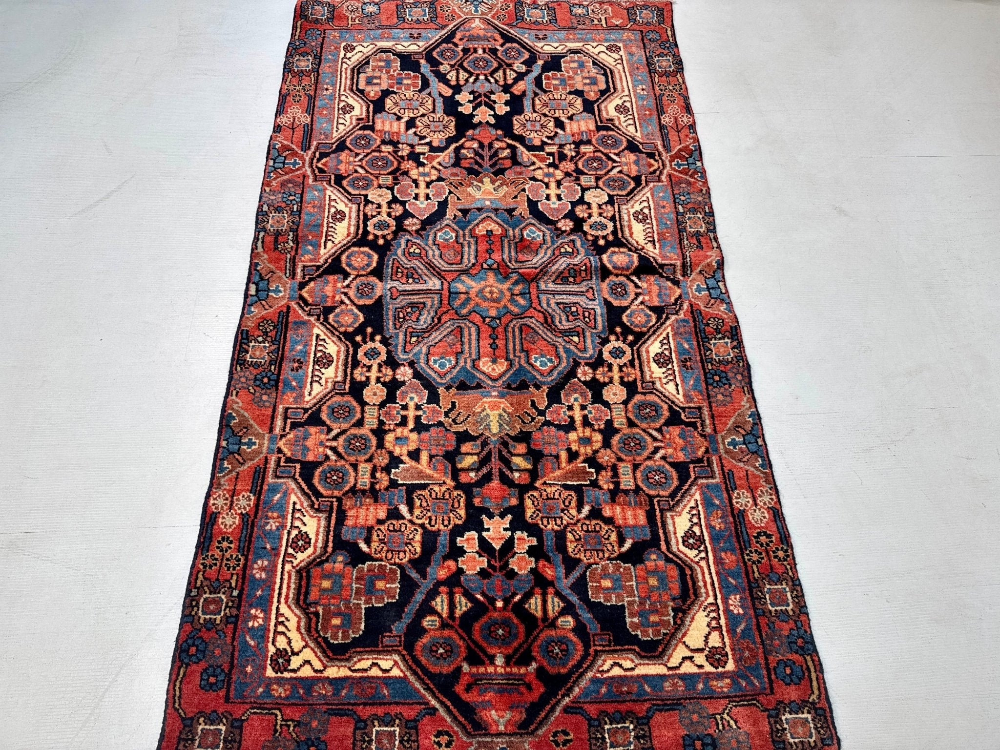 Persian Nahavand rug with navy field, red medallions, and cream border details.