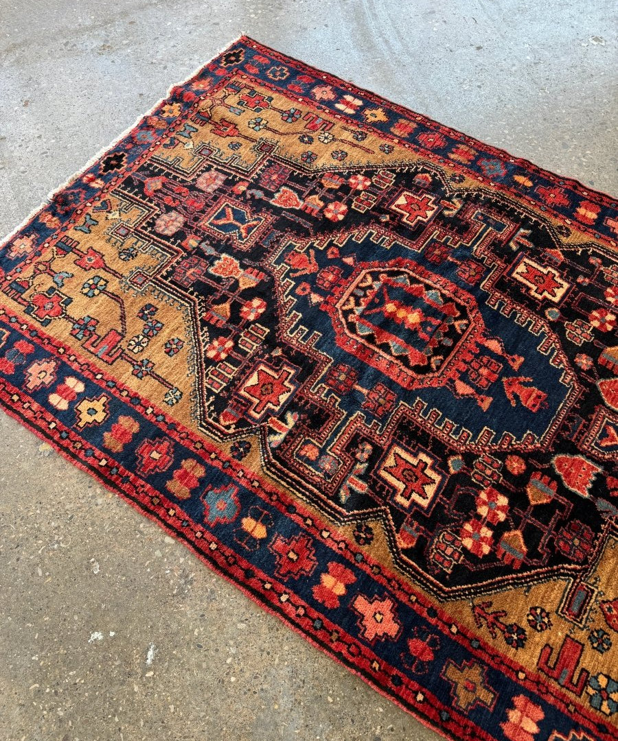 Geometric patterned Persian rug with navy field, red trim, beige blocks, and corner details.