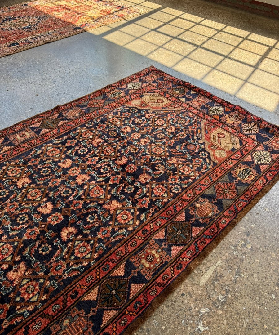 Nahavand-style Persian rug with navy floral center and red border on a tiled floor
