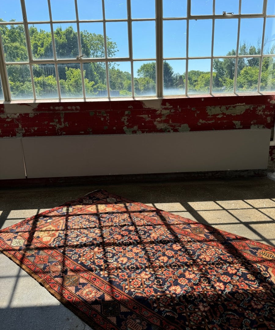 Nahavand-style rug with red and navy floral pattern, shown folded on the floor