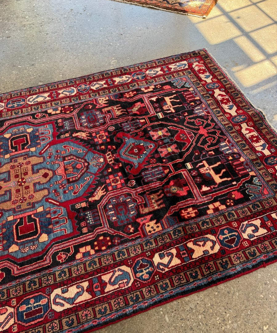 Persian area rug angled view with navy field, red motifs, and cream-trimmed edges