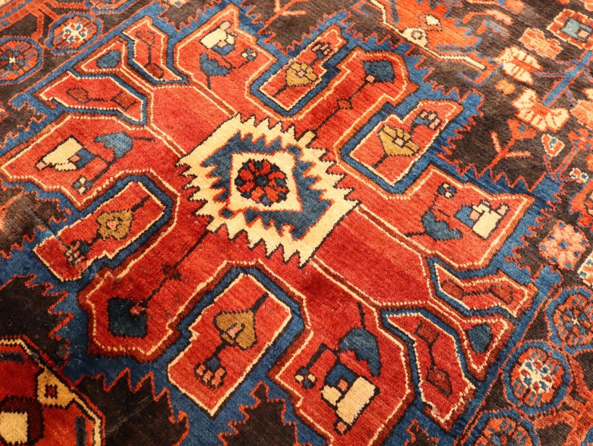 Persian-style rug close-up with red center, cream shapes, and black outlines with blue accents