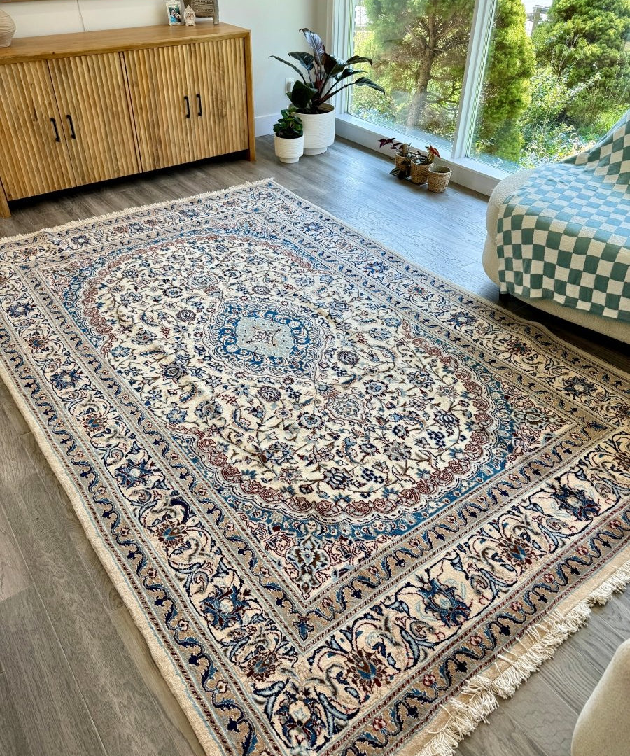Persian-style area rug with cream field, blue scrolling motifs, and fringed border
