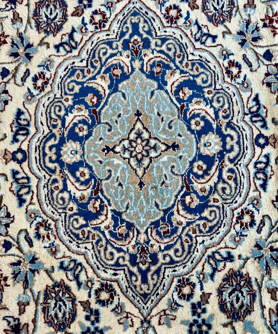 Persian-style rug close-up of central blue medallion on cream background