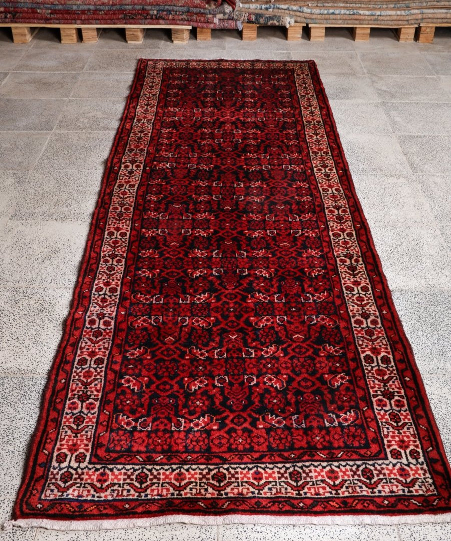 Persian runner rug with dark red field, black pattern, cream border and fringe.