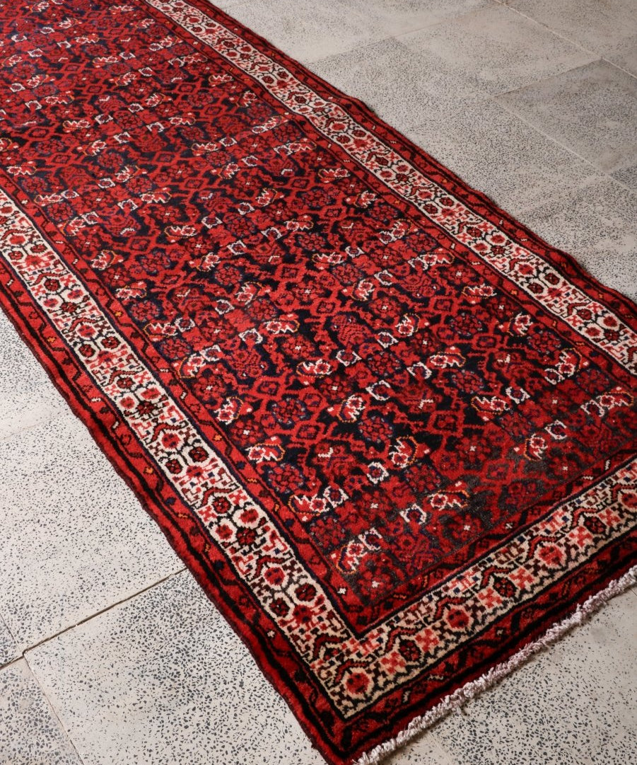 Persian runner rug angled view with dark red center, cream border stripe, and black edge.