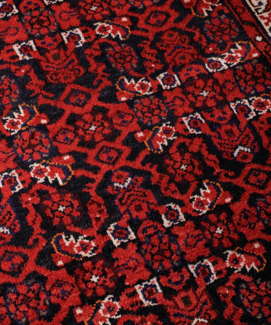 Persian runner rug close-up: dark red and black geometric motifs with cream accents.