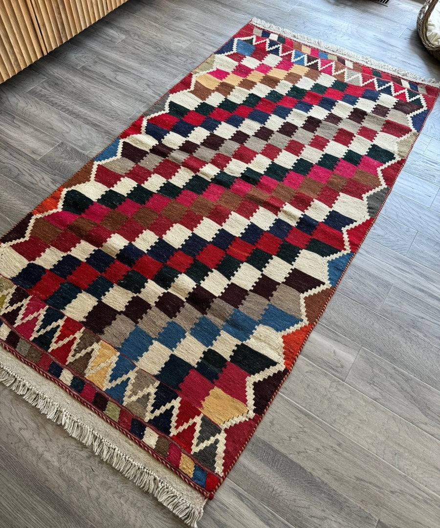 Persian Qashqai kilim rug laid diagonally, red blue beige geometric pattern, fringed ends