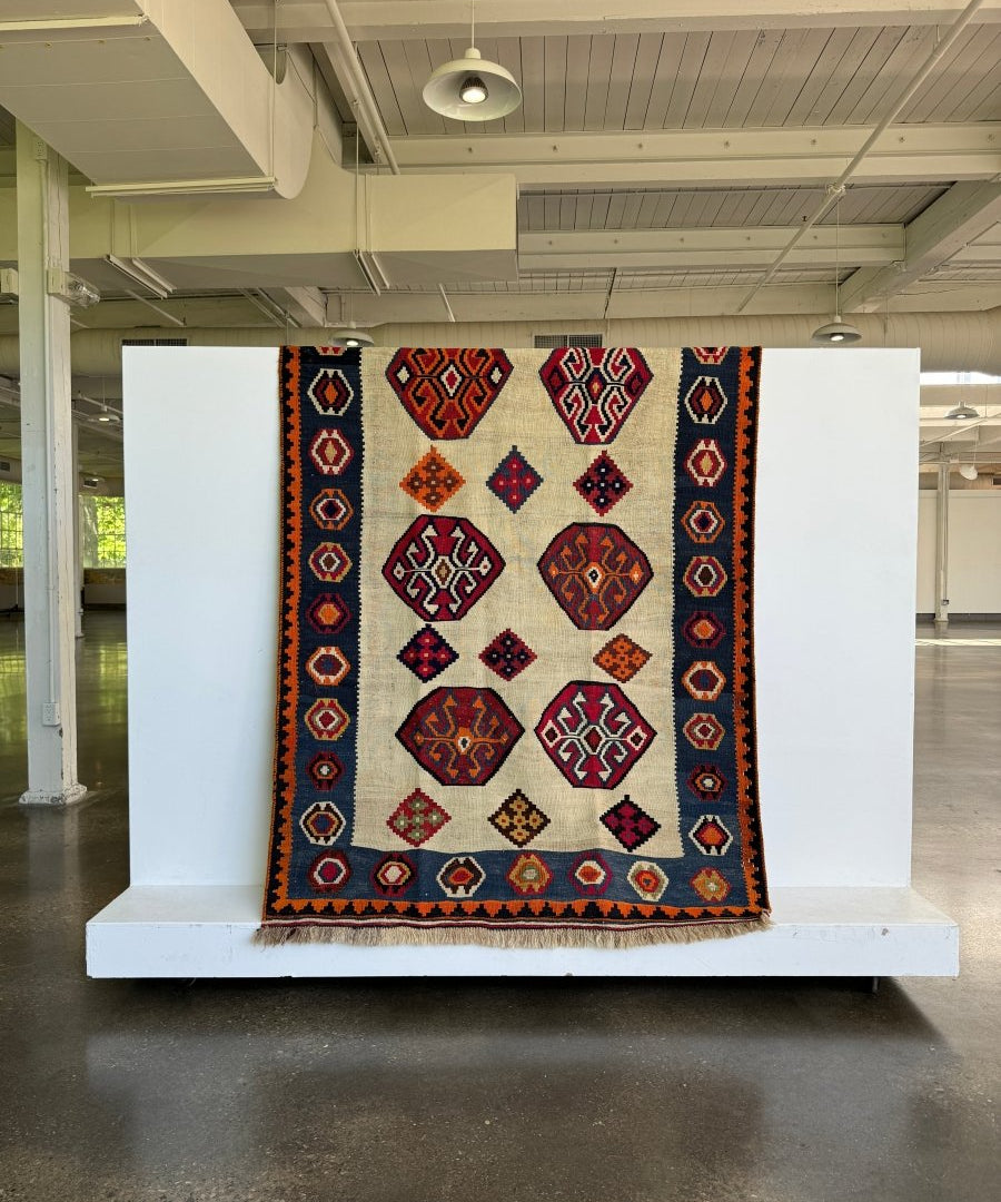 Kilim rug fully shown with cream field, navy frame, and red-orange repeating diamond motifs