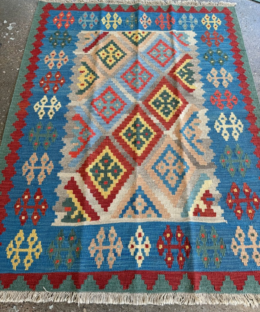 Colorful Persian-style kilim rug with blue field, red accents, geometric diamond pattern